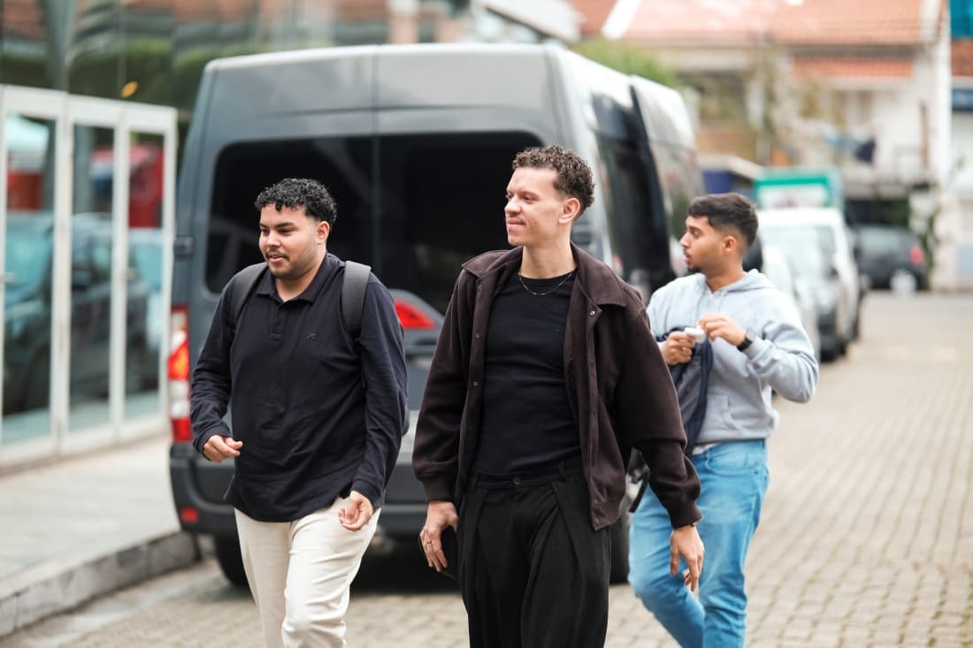 Três homens jovens saindo de uma vã em frente a um prédio. Estão agasalhados